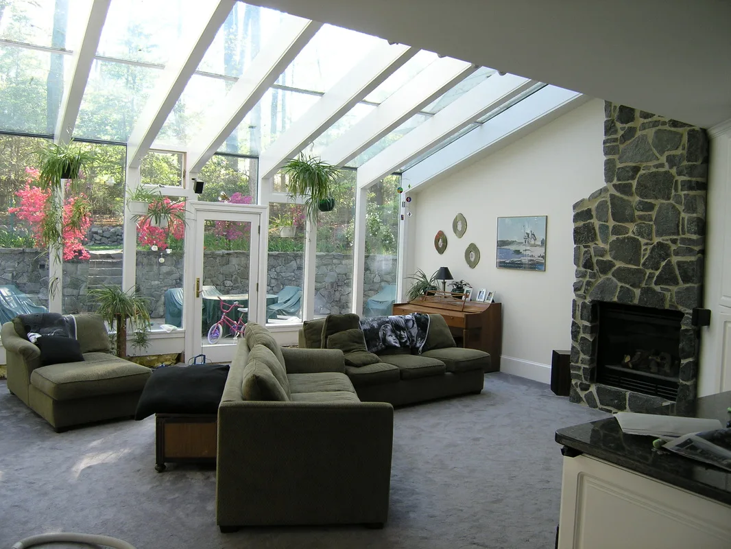 Sunroom addition with full glass roof, stone fireplace and garden view